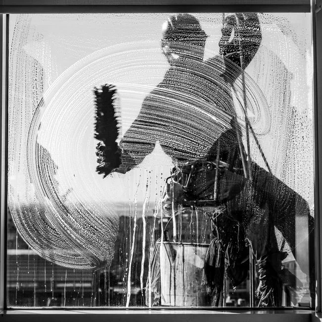 A man cleaning a glass door indoors using a spray bottle and cloth.